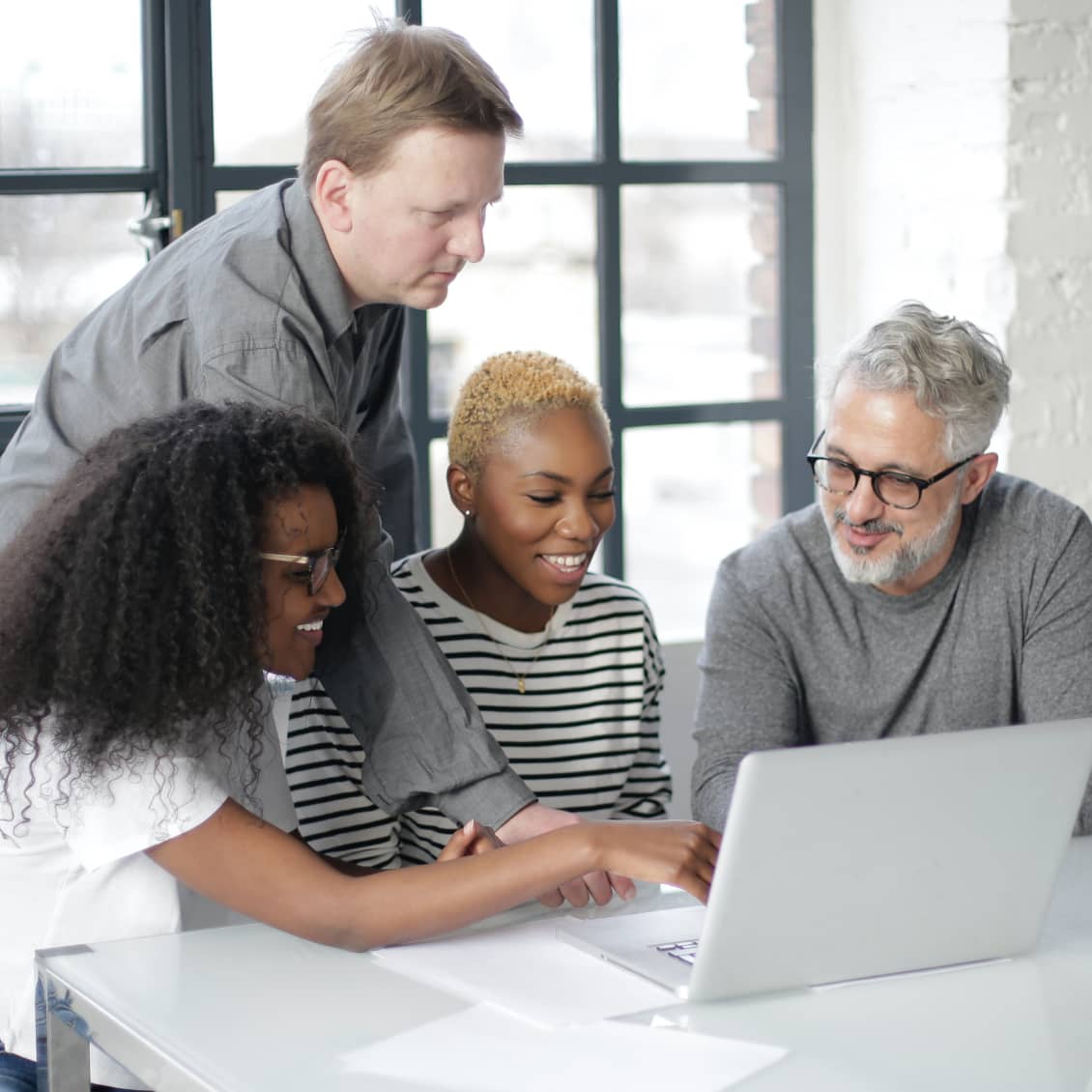 Teamwork group of co-workers gathered around laptop in office setting