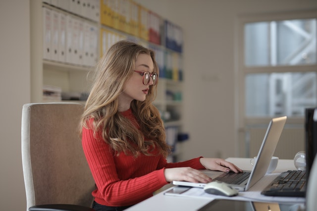 woman in red shirt and glasses looking at laptop in home office